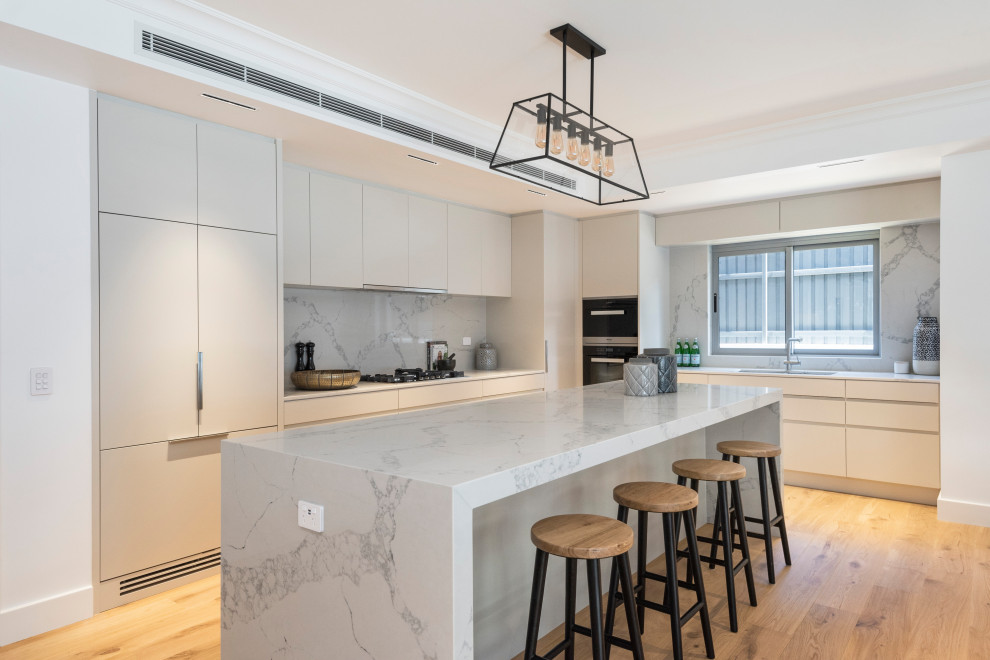 Large contemporary l-shaped kitchen in Sydney with a double-bowl sink, flat-panel cabinets, grey cabinets, marble benchtops, marble splashback, stainless steel appliances, light hardwood floors, with island and white benchtop.