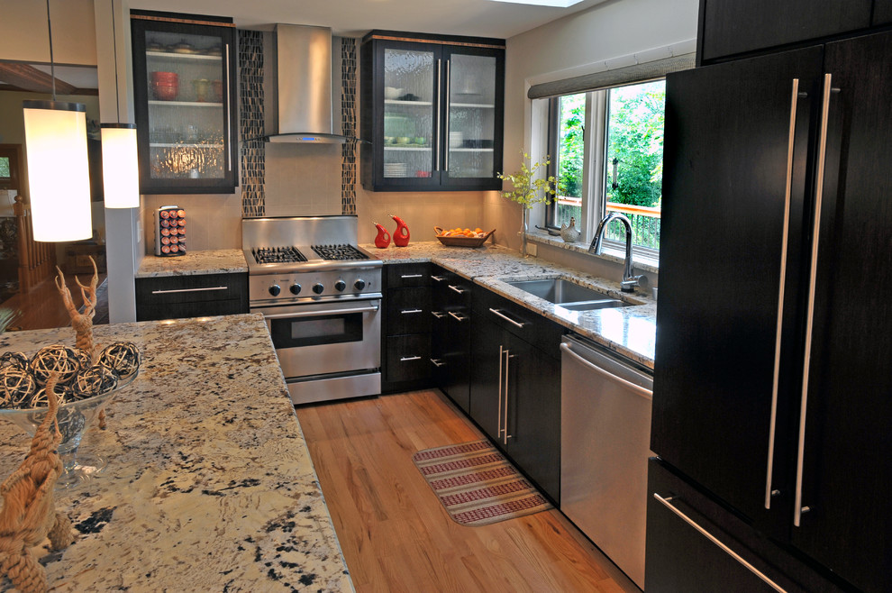 Inspiration for a mid-sized transitional galley light wood floor enclosed kitchen remodel in Milwaukee with an undermount sink, flat-panel cabinets, black cabinets, granite countertops, beige backsplash, mosaic tile backsplash, stainless steel appliances and beige walls