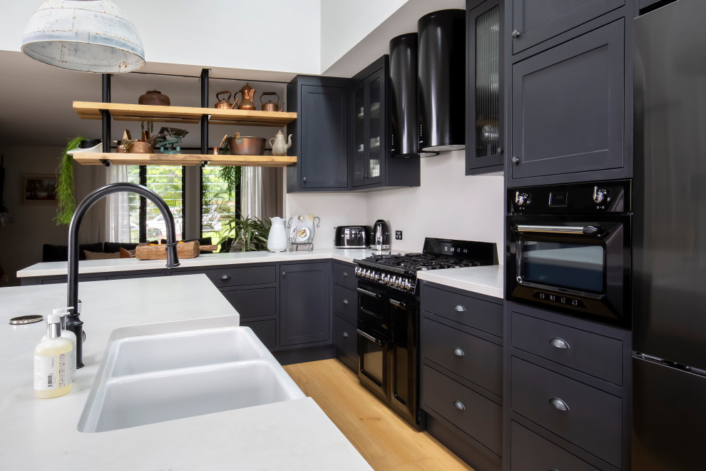 Design ideas for a large transitional l-shaped open plan kitchen in Sydney with a farmhouse sink, shaker cabinets, black cabinets, quartz benchtops, white splashback, engineered quartz splashback, black appliances, light hardwood floors, with island, white benchtop and vaulted.