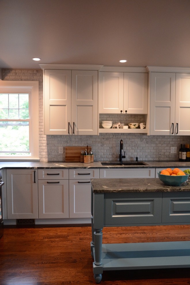 Mid-sized transitional l-shaped dark wood floor eat-in kitchen photo with an undermount sink, gray cabinets, soapstone countertops, gray backsplash, stone tile backsplash, stainless steel appliances, an island and shaker cabinets