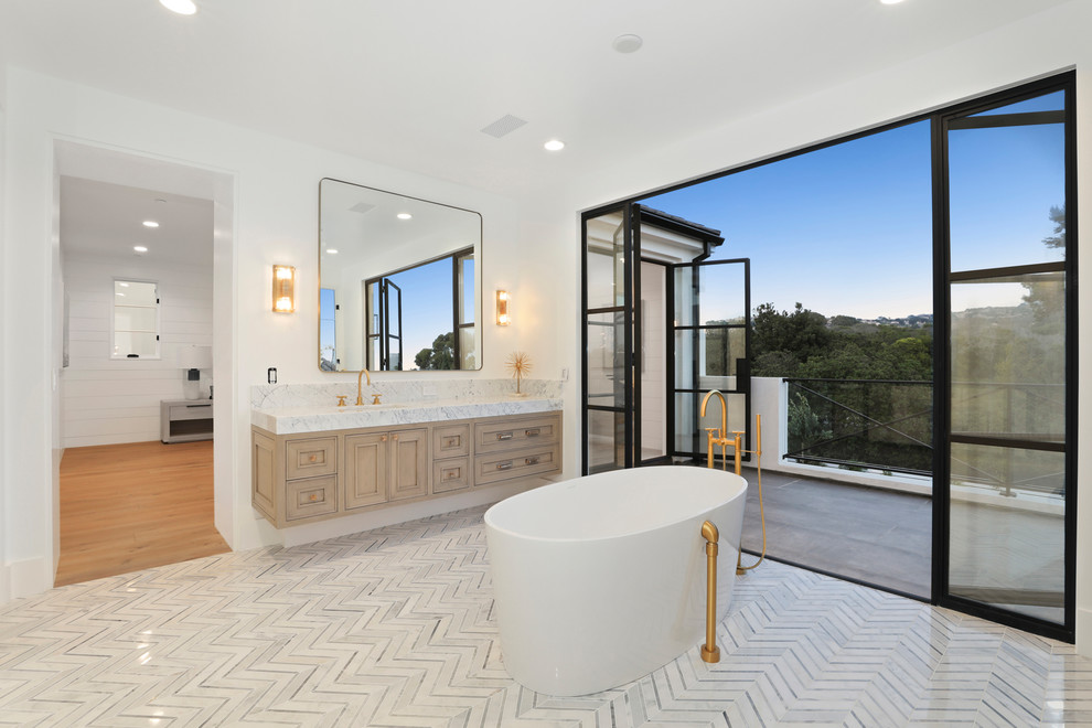 Inspiration for a large modern master bathroom in Orange County with recessed-panel cabinets, light wood cabinets, a freestanding tub, a one-piece toilet, gray tile, marble, white walls, a drop-in sink, marble benchtops, grey floor, an alcove shower, marble floors and an open shower.