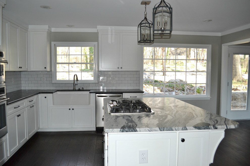 Large transitional l-shaped dark wood floor open concept kitchen photo with a farmhouse sink, shaker cabinets, white cabinets, marble countertops, white backsplash, subway tile backsplash, stainless steel appliances and an island