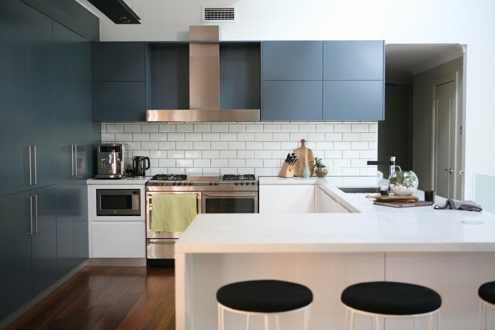 Contemporary u-shaped kitchen in Sydney with an undermount sink, flat-panel cabinets, blue cabinets, white splashback, subway tile splashback, stainless steel appliances, dark hardwood floors, a peninsula, brown floor and white benchtop.