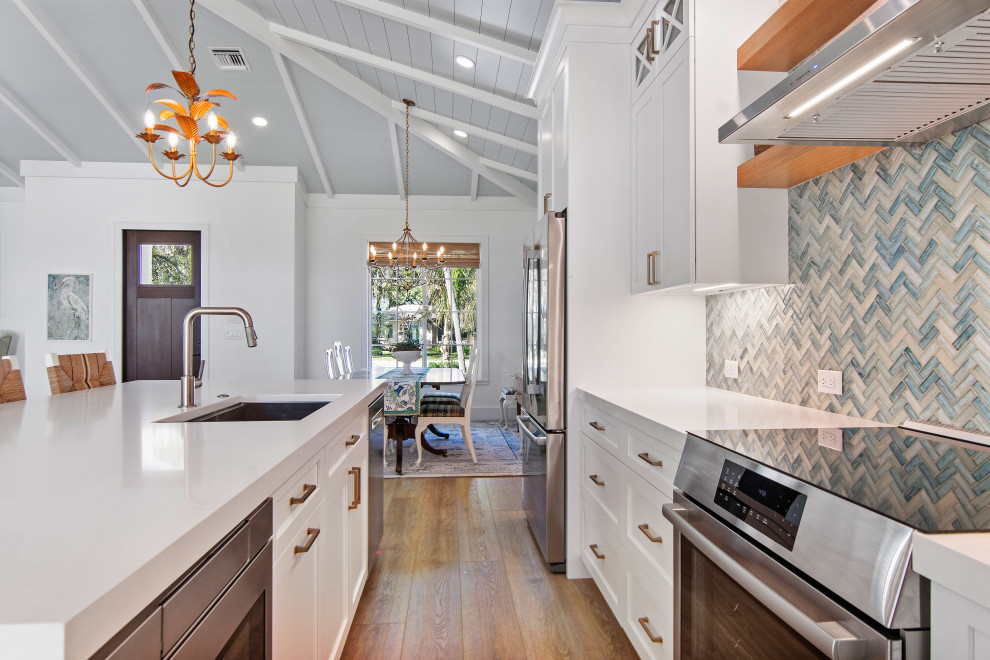 This is an example of a large beach style single-wall eat-in kitchen with a drop-in sink, beaded inset cabinets, white cabinets, marble benchtops, mosaic tile splashback, stainless steel appliances, vinyl floors, with island, beige floor, white benchtop, timber and blue splashback.