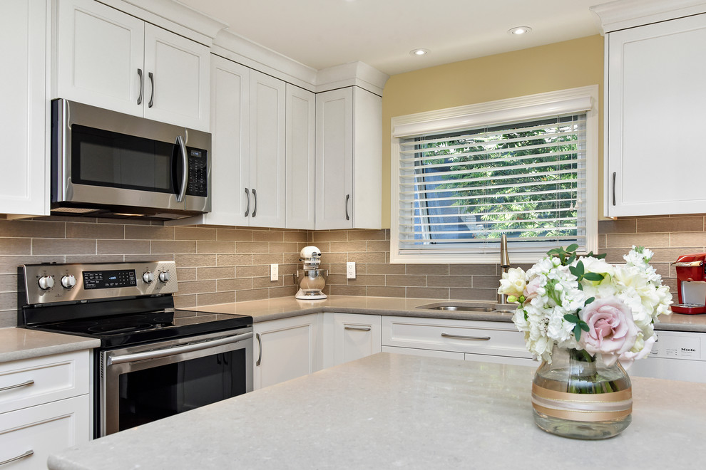 This is an example of a mid-sized transitional l-shaped eat-in kitchen in Calgary with an undermount sink, recessed-panel cabinets, white cabinets, quartz benchtops, grey splashback, glass tile splashback, stainless steel appliances, medium hardwood floors, with island and beige floor.