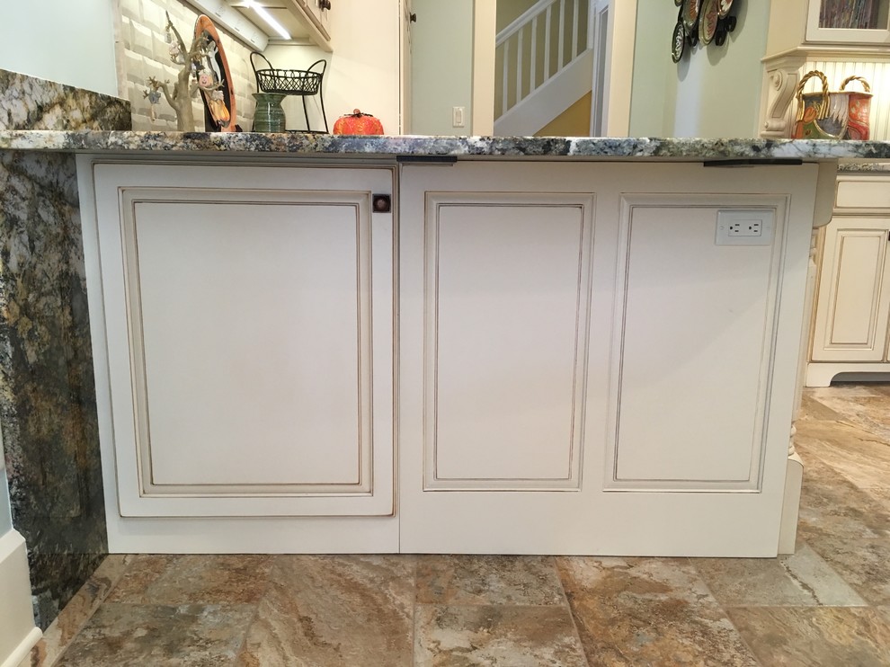 Example of a large transitional galley porcelain tile enclosed kitchen design with an undermount sink, raised-panel cabinets, distressed cabinets, granite countertops, beige backsplash, stone tile backsplash, stainless steel appliances and a peninsula