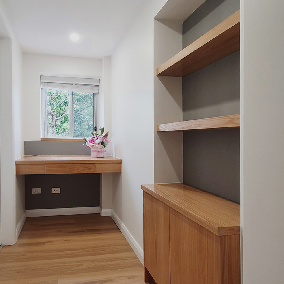 Idee per un piccolo ufficio minimalista con pareti bianche, pavimento in laminato, scrivania incassata e pavimento marrone