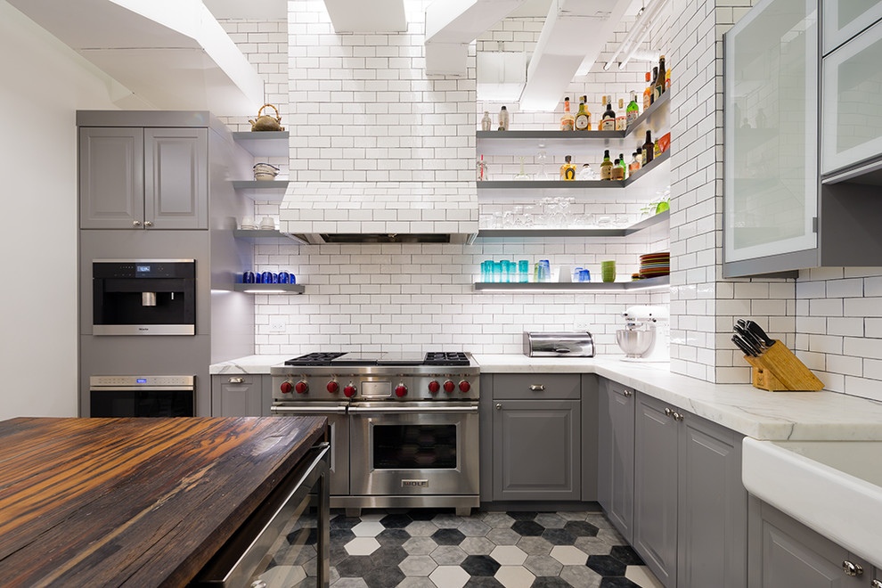 Mid-sized industrial kitchen in New York with marble benchtops, white splashback, ceramic floors, with island, a farmhouse sink, raised-panel cabinets, grey cabinets, subway tile splashback, stainless steel appliances and multi-coloured floor.
