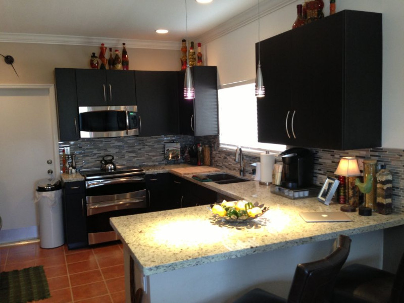 Eat-in kitchen - mid-sized u-shaped terra-cotta tile eat-in kitchen idea in Miami with a double-bowl sink, flat-panel cabinets, black cabinets, stainless steel countertops, gray backsplash, matchstick tile backsplash, stainless steel appliances and no island