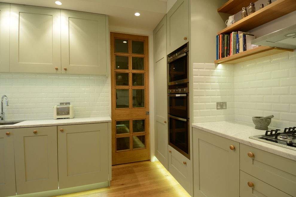 Inspiration for a small scandinavian u-shaped separate kitchen in London with an integrated sink, shaker cabinets, green cabinets, marble benchtops, white splashback, subway tile splashback, stainless steel appliances, light hardwood floors and no island.