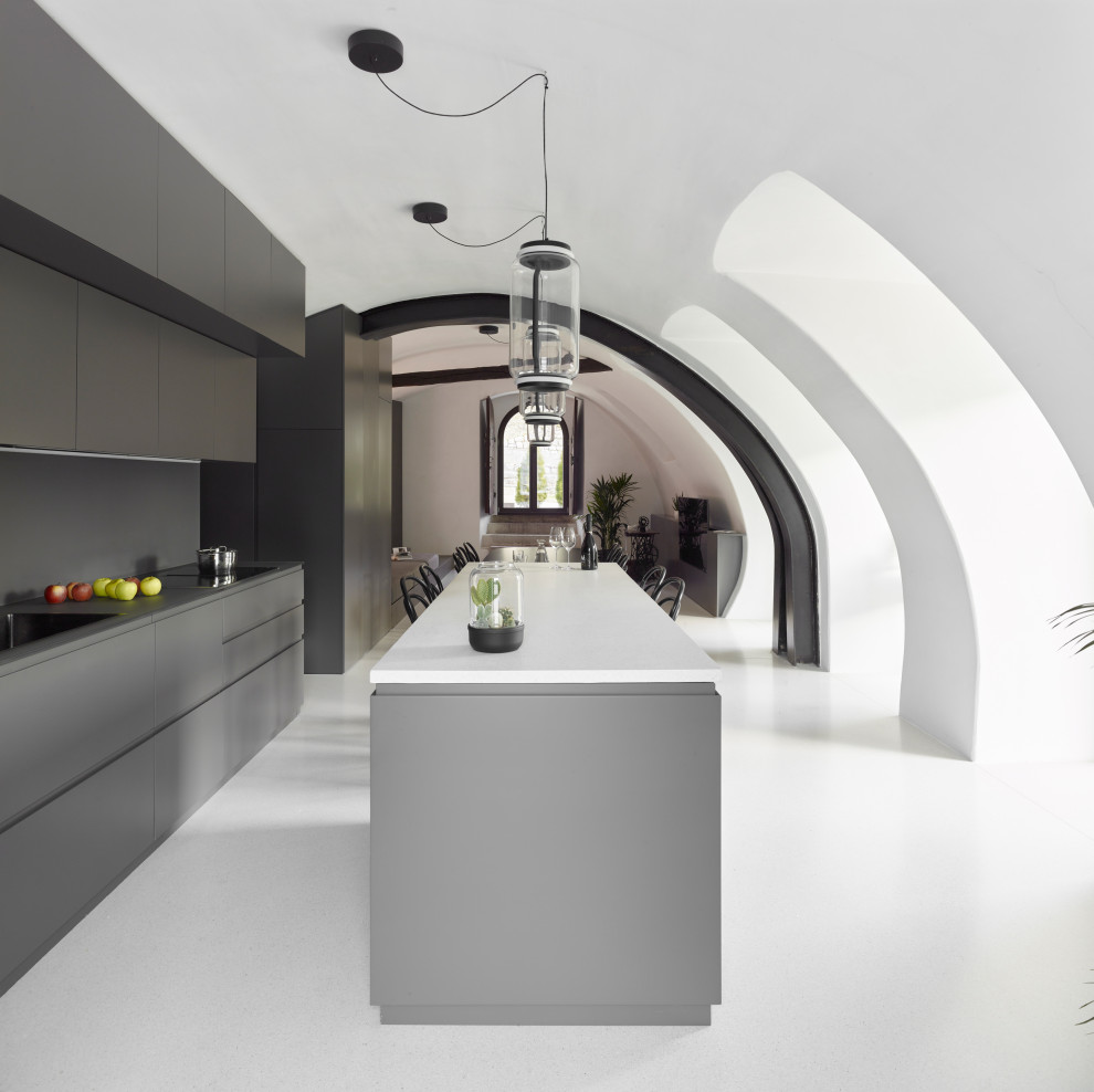 Expansive contemporary galley open plan kitchen in Other with a submerged sink, flat-panel cabinets, grey cabinets, terrazzo worktops, black appliances, terrazzo flooring, an island, white worktops and a vaulted ceiling.