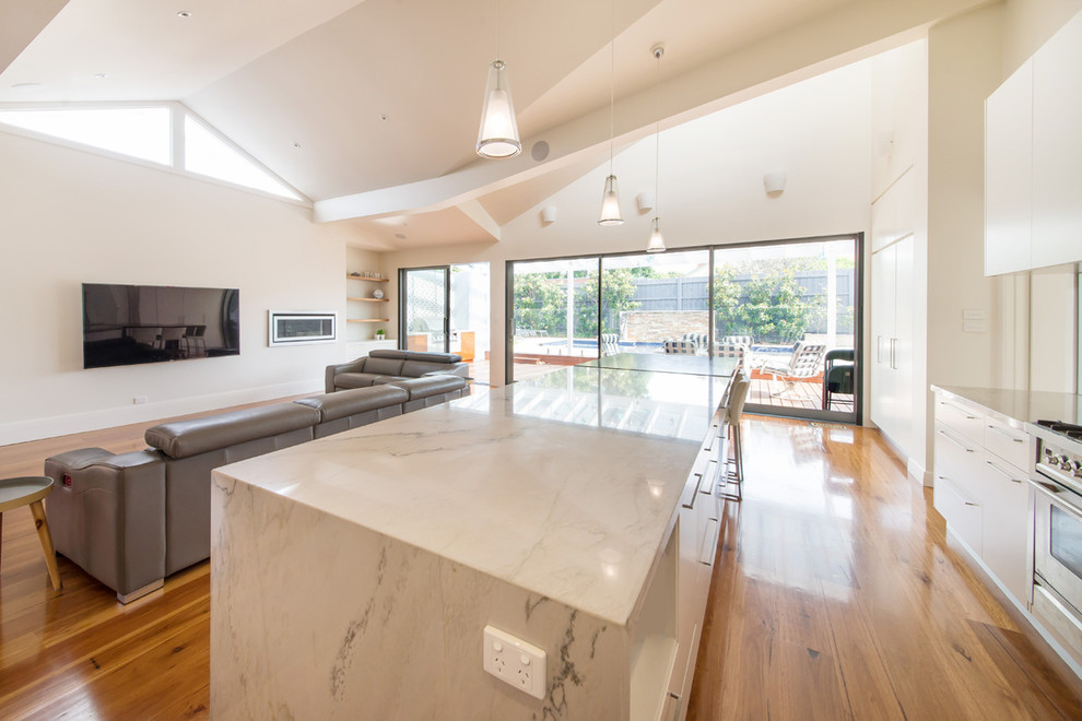 Photo of a large contemporary u-shaped open plan kitchen in Melbourne with medium hardwood floors, brown floor, an undermount sink, flat-panel cabinets, white cabinets, quartz benchtops, metallic splashback, glass sheet splashback, stainless steel appliances and with island.