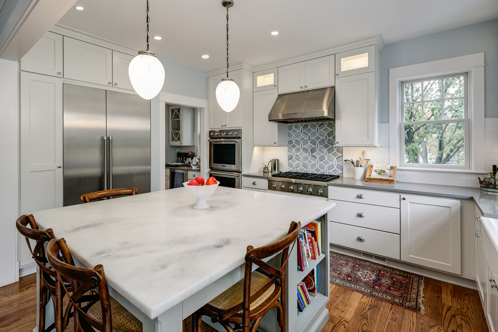 Mid-sized traditional u-shaped eat-in kitchen in Orange County with a farmhouse sink, shaker cabinets, white cabinets, marble benchtops, white splashback, subway tile splashback, stainless steel appliances, medium hardwood floors and with island.