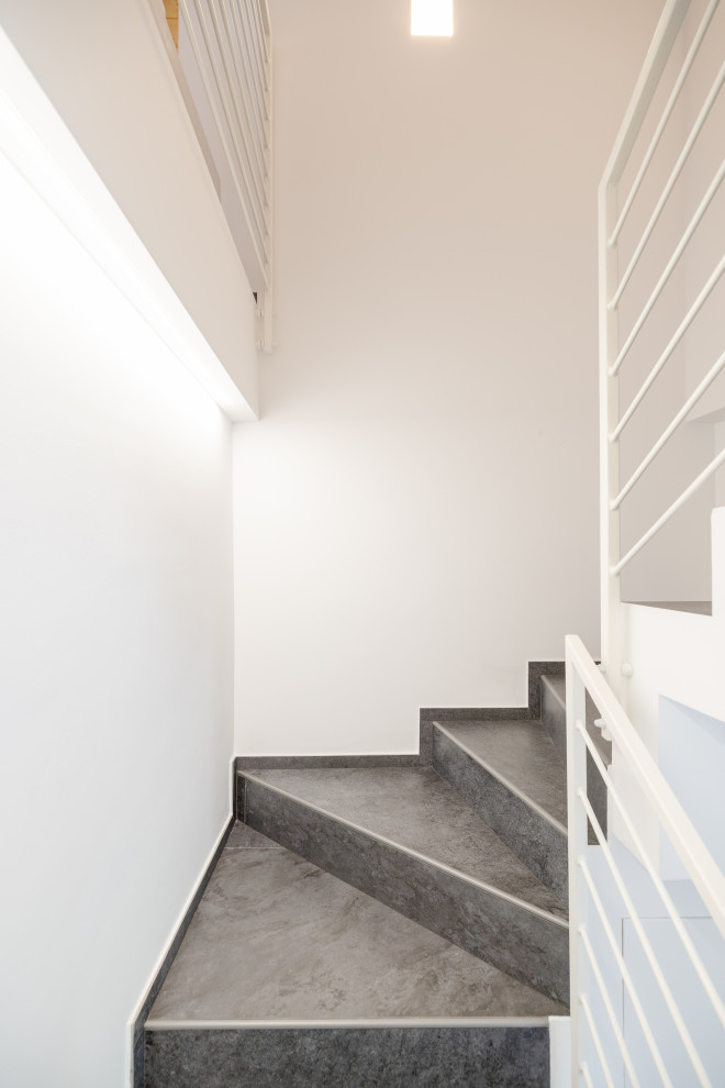 Kleine Moderne Treppe in U-Form mit gefliesten Treppenstufen, gefliesten Setzstufen und Stahlgeländer in Mailand