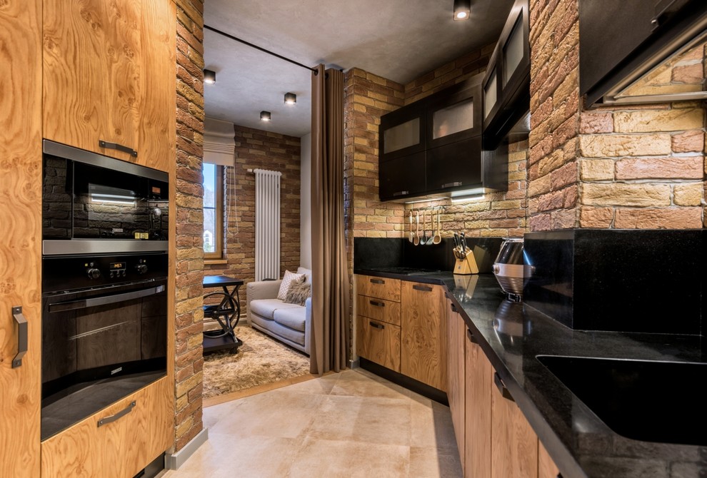 Photo of an industrial l-shaped kitchen in Other with an integrated sink, flat-panel cabinets, medium wood cabinets, black splashback, black appliances, beige floor and black benchtop.