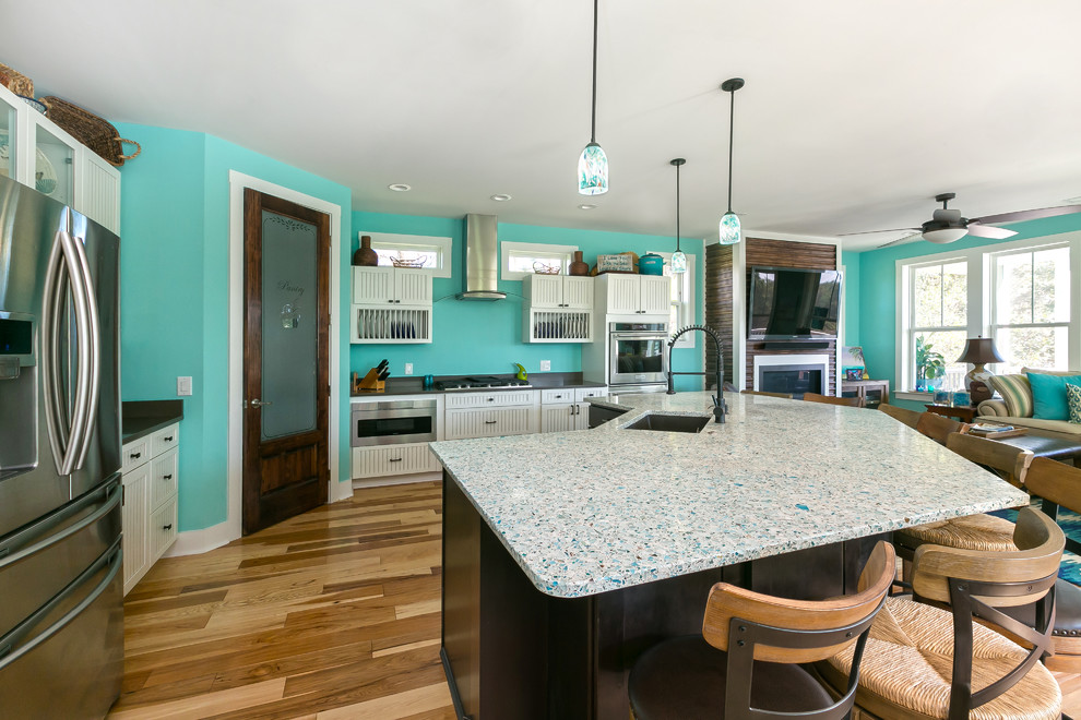 Large beach style l-shaped open plan kitchen in Charleston with an undermount sink, white cabinets, recycled glass benchtops, blue splashback, black appliances, dark hardwood floors and with island.