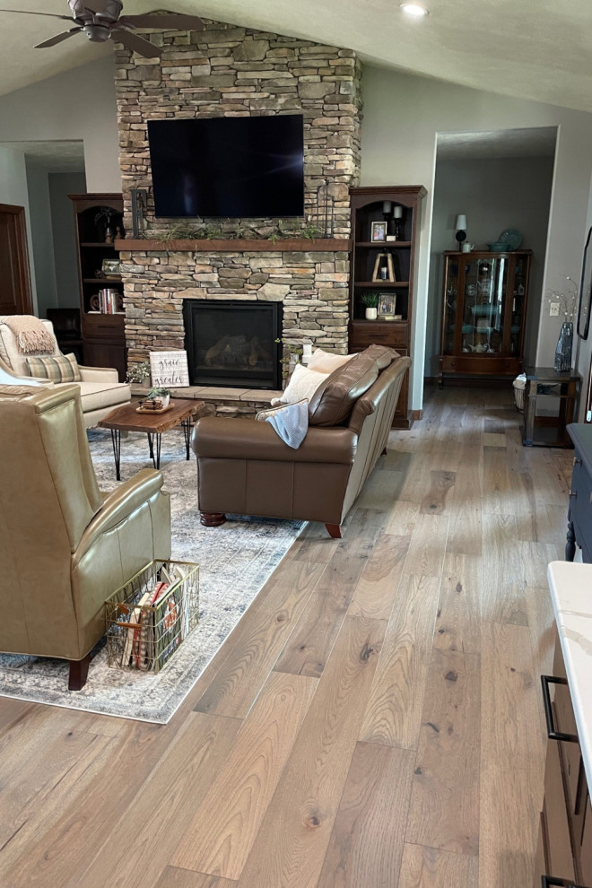 This is an example of a large formal open plan living room in Other with grey walls, medium hardwood flooring, a standard fireplace, a stone fireplace surround, a wall mounted tv, multi-coloured floors, a vaulted ceiling and panelled walls.