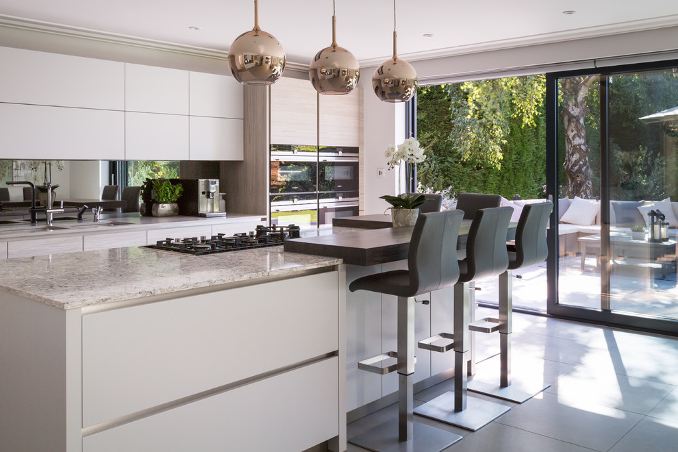 This is an example of a large contemporary l-shaped kitchen in Gloucestershire with an undermount sink, flat-panel cabinets, light wood cabinets, solid surface benchtops, metallic splashback, mirror splashback, stainless steel appliances, porcelain floors, with island, grey floor and grey benchtop.