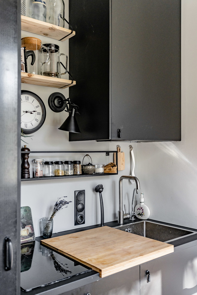 This is an example of an industrial single-wall kitchen in Moscow with a drop-in sink, flat-panel cabinets, grey cabinets, white splashback and black benchtop.