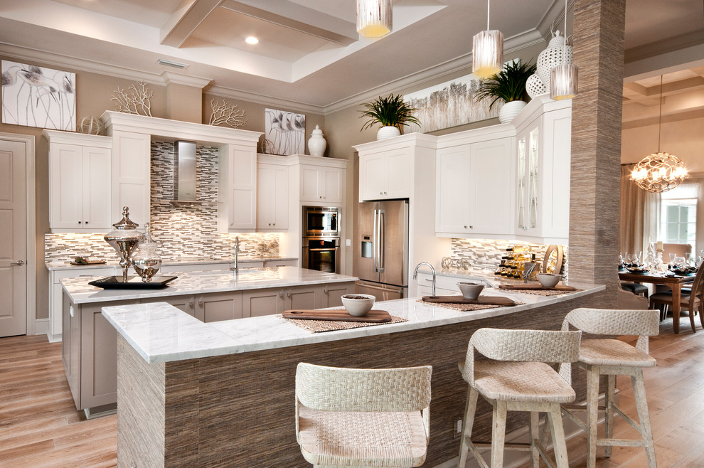 Design ideas for a beach style u-shaped kitchen in Miami with shaker cabinets, white cabinets, multi-coloured splashback, mosaic tile splashback, stainless steel appliances, light hardwood floors and multiple islands.