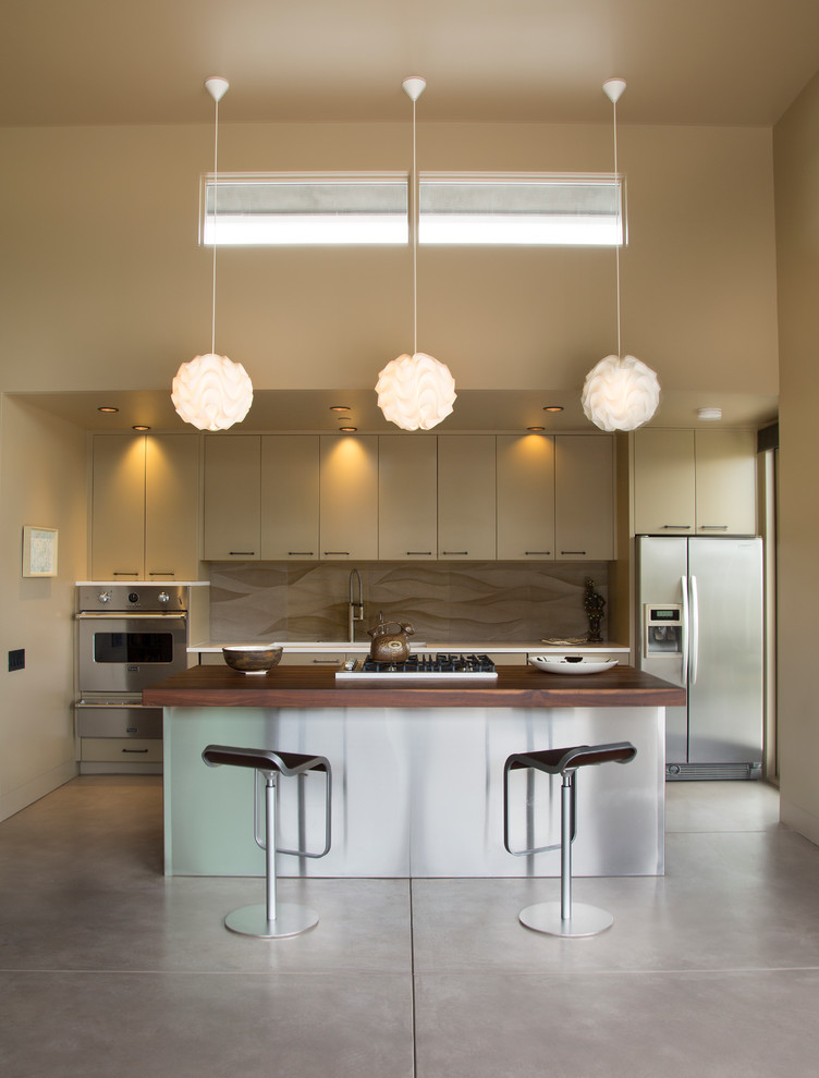 Large contemporary galley eat-in kitchen in Santa Barbara with flat-panel cabinets, beige cabinets, wood benchtops, beige splashback, stainless steel appliances, ceramic splashback, concrete floors and with island.