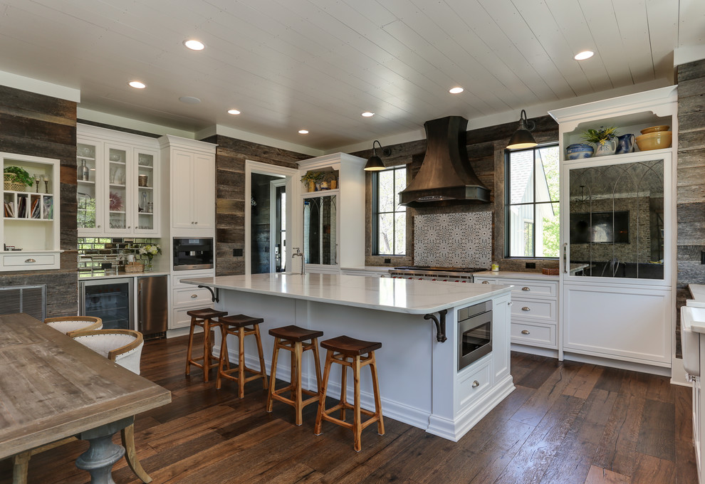 This is an example of a large country eat-in kitchen in Raleigh with white cabinets, quartz benchtops, with island, brown floor, white benchtop, shaker cabinets, multi-coloured splashback, stainless steel appliances and dark hardwood floors.