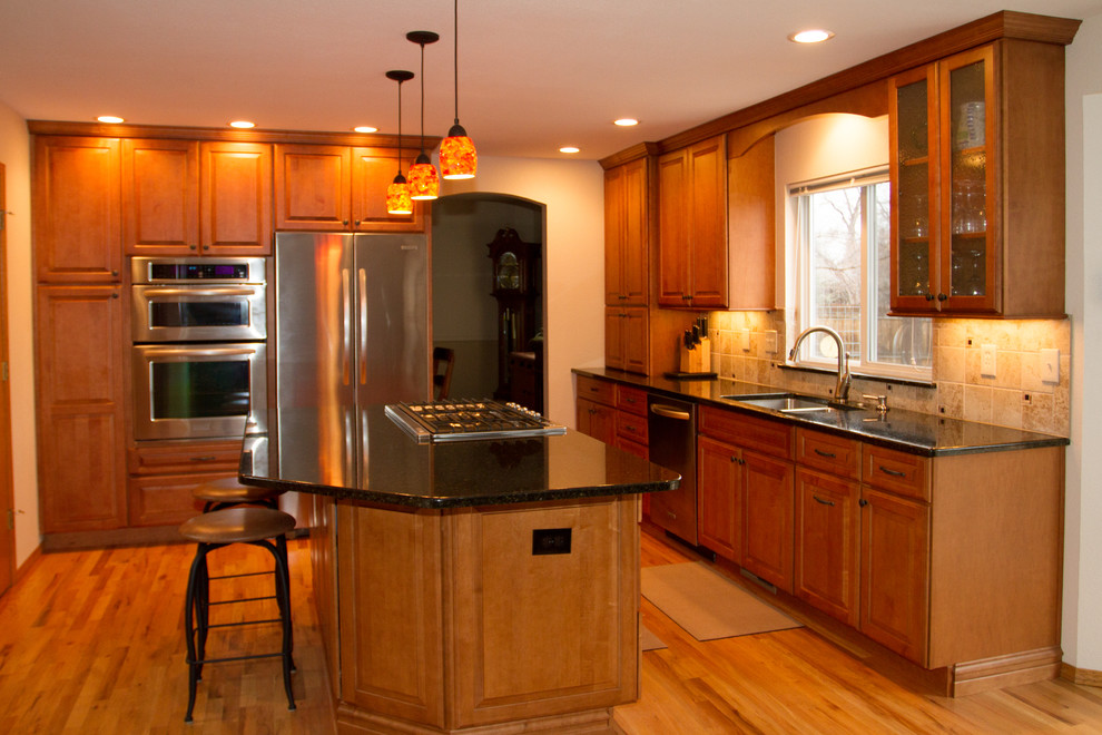 Mid-sized transitional l-shaped light wood floor and brown floor open concept kitchen photo in Denver with a double-bowl sink, raised-panel cabinets, medium tone wood cabinets, granite countertops, beige backsplash, stone tile backsplash, stainless steel appliances and an island