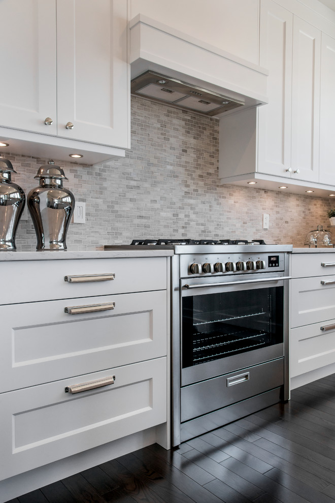 This is an example of a mid-sized transitional l-shaped eat-in kitchen in Calgary with recessed-panel cabinets, white cabinets, quartz benchtops, multi-coloured splashback, mosaic tile splashback, stainless steel appliances, dark hardwood floors and with island.
