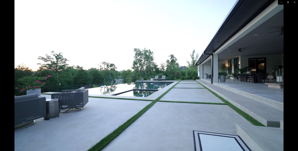 Inspiration for a large modern back rectangular infinity hot tub in Dallas with concrete slabs.