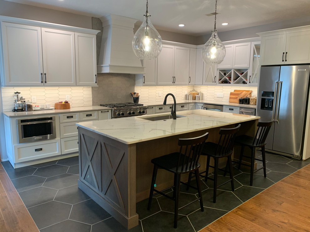 Photo of a large transitional l-shaped eat-in kitchen in Other with a farmhouse sink, recessed-panel cabinets, white cabinets, quartz benchtops, multi-coloured splashback, ceramic splashback, stainless steel appliances, ceramic floors, with island, black floor and white benchtop.