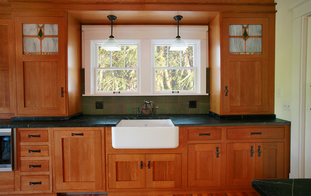 This is an example of an arts and crafts u-shaped eat-in kitchen in Tampa with a farmhouse sink, shaker cabinets, medium wood cabinets, green splashback and stainless steel appliances.