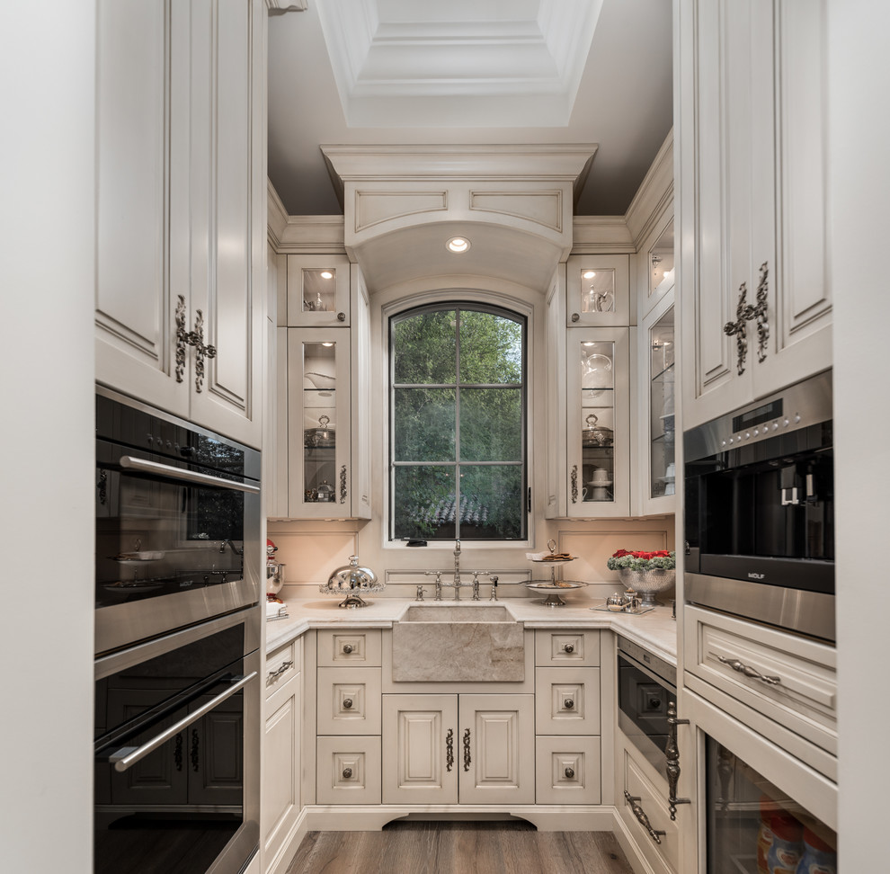 Inspiration for an expansive traditional u-shaped separate kitchen in Phoenix with a farmhouse sink, raised-panel cabinets, light wood cabinets, quartzite benchtops, beige splashback, porcelain splashback, stainless steel appliances, medium hardwood floors, no island, brown floor and beige benchtop.