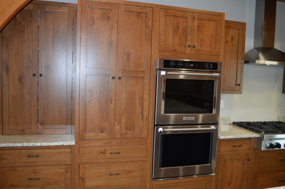 Example of a mid-sized mountain style u-shaped medium tone wood floor, brown floor and exposed beam eat-in kitchen design with a farmhouse sink, shaker cabinets, medium tone wood cabinets, paneled appliances and an island