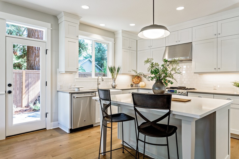 Transitional kitchen in Portland with a farmhouse sink, shaker cabinets, white cabinets, white splashback, subway tile splashback, stainless steel appliances, light hardwood floors and with island.