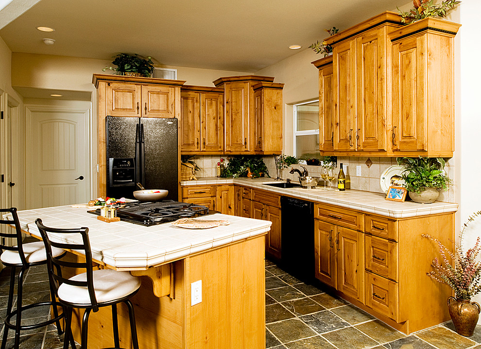 Inspiration for a small rustic l-shaped slate floor eat-in kitchen remodel with an undermount sink, raised-panel cabinets, medium tone wood cabinets, tile countertops, beige backsplash, porcelain backsplash, black appliances and an island