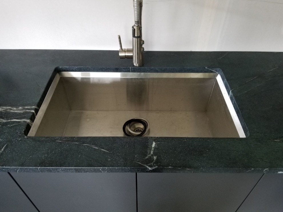 Inspiration for a modern u-shaped ceramic tile and beige floor eat-in kitchen remodel with an undermount sink, flat-panel cabinets, white cabinets, soapstone countertops, stainless steel appliances, a peninsula and black countertops