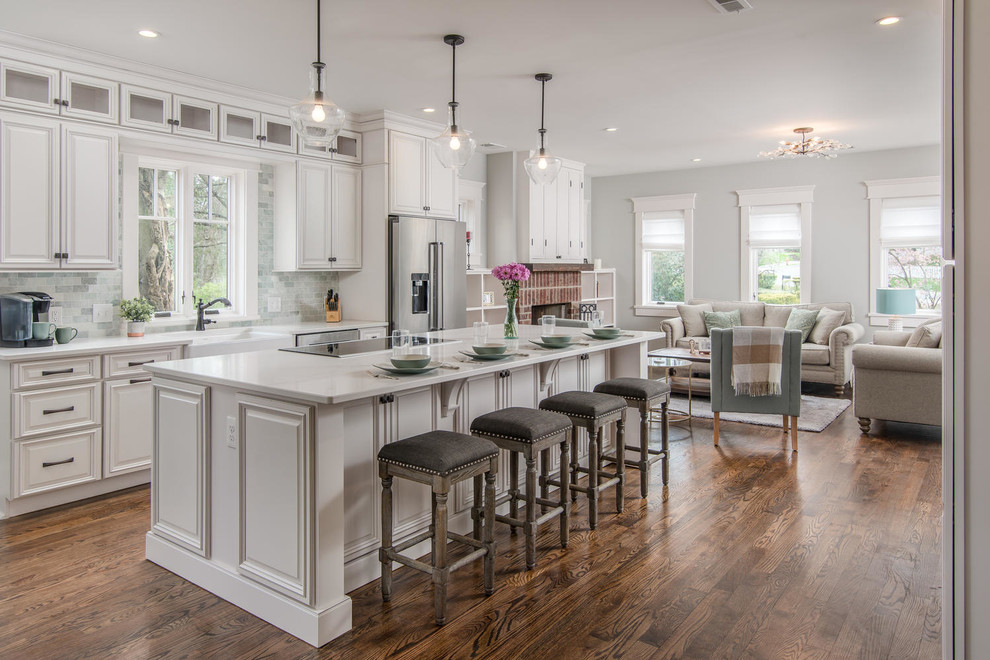 Photo of a large arts and crafts open plan kitchen in Nashville with a farmhouse sink, raised-panel cabinets, white cabinets, quartzite benchtops, green splashback, marble splashback, stainless steel appliances, medium hardwood floors, with island, brown floor and white benchtop.