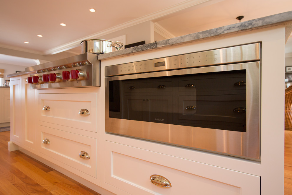 Home design - transitional medium tone wood floor home design idea in Boston with a farmhouse sink, recessed-panel cabinets, white cabinets, granite countertops, white backsplash, subway tile backsplash, stainless steel appliances and two islands