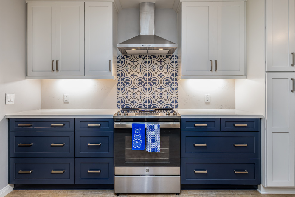 Design ideas for a medium sized beach style l-shaped kitchen in San Diego with a belfast sink, shaker cabinets, blue cabinets, engineered stone countertops, blue splashback, porcelain splashback, stainless steel appliances, light hardwood flooring and white worktops.