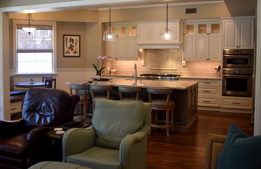 Mid-sized transitional l-shaped dark wood floor and brown floor open concept kitchen photo in Houston with a farmhouse sink, raised-panel cabinets, white cabinets, quartzite countertops, beige backsplash, ceramic backsplash, stainless steel appliances, an island and white countertops