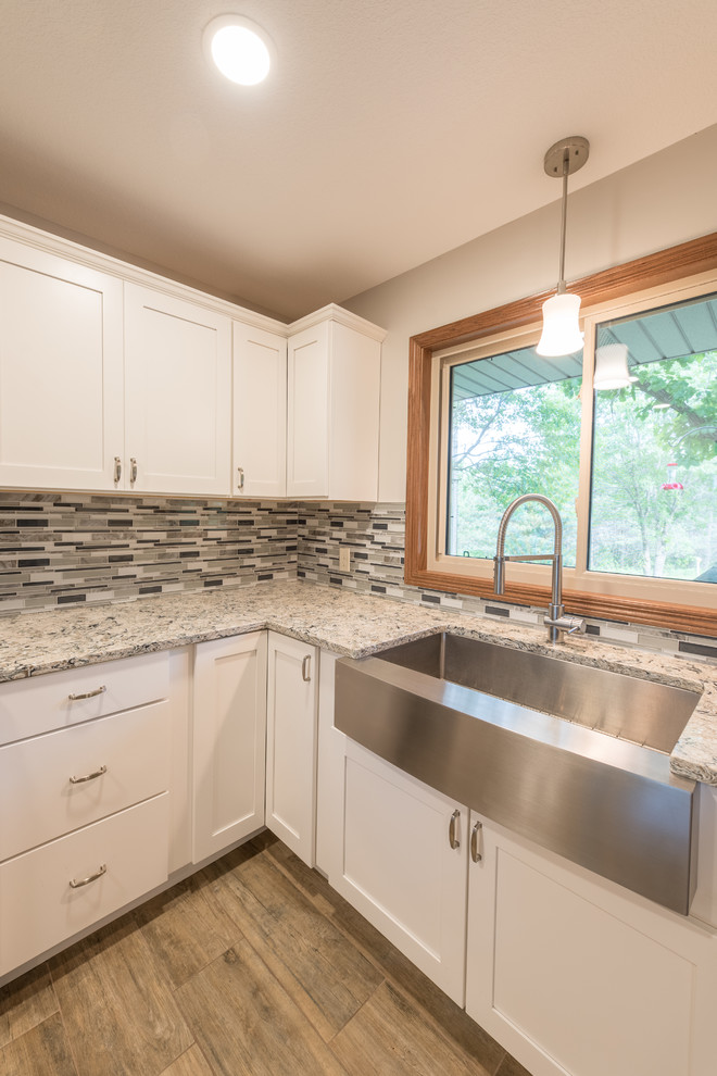 Example of a mid-sized transitional l-shaped medium tone wood floor and brown floor eat-in kitchen design in Minneapolis with a farmhouse sink, shaker cabinets, white cabinets, granite countertops, multicolored backsplash, matchstick tile backsplash, stainless steel appliances, an island and gray countertops