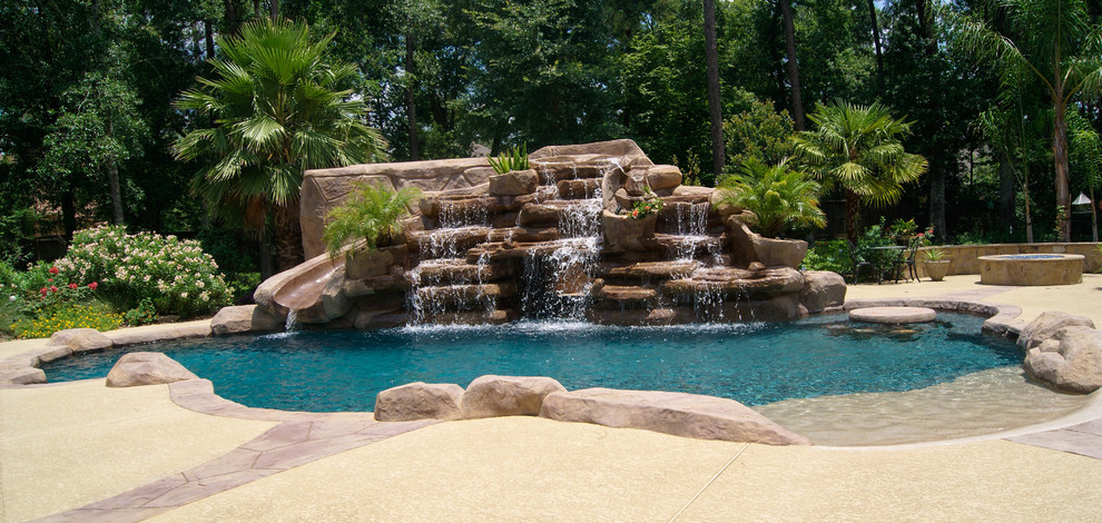 Inspiration for a mid-sized tropical backyard custom-shaped natural pool in Houston with a water slide and stamped concrete.