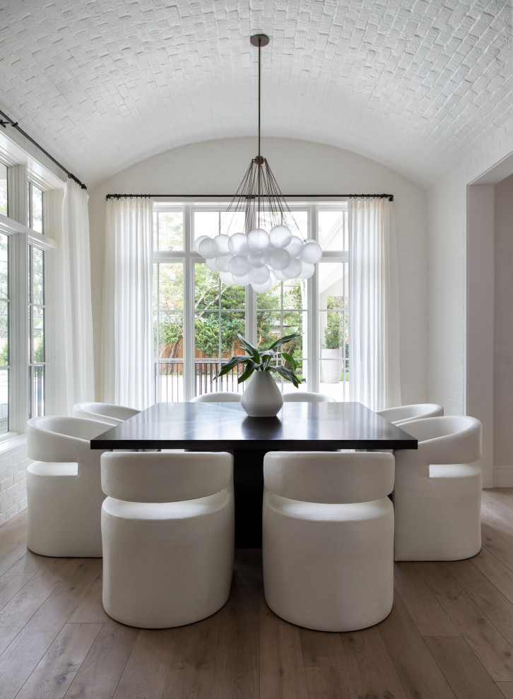 This is an example of an expansive transitional separate dining room in Houston with white walls, medium hardwood floors, brown floor, vaulted and brick walls.