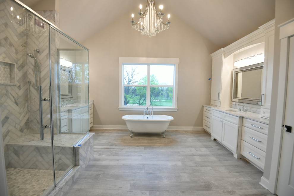Klassisk inredning av ett vit vitt badrum, med luckor med infälld panel, vita skåp, ett badkar med tassar, en dubbeldusch, vit kakel, marmorkakel, vita väggar, klinkergolv i keramik, ett undermonterad handfat, marmorbänkskiva, grått golv och dusch med gångjärnsdörr