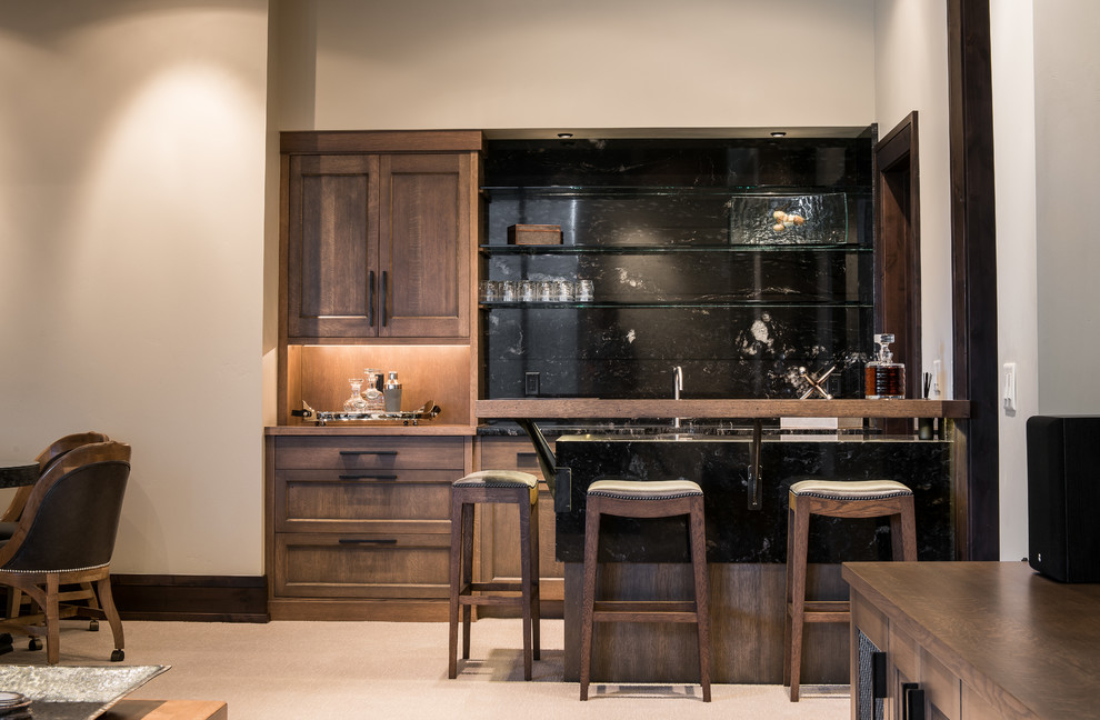 Photo of a mid-sized transitional single-wall seated home bar in Other with granite benchtops, stone slab splashback, shaker cabinets, dark wood cabinets, black splashback, carpet and beige floor.