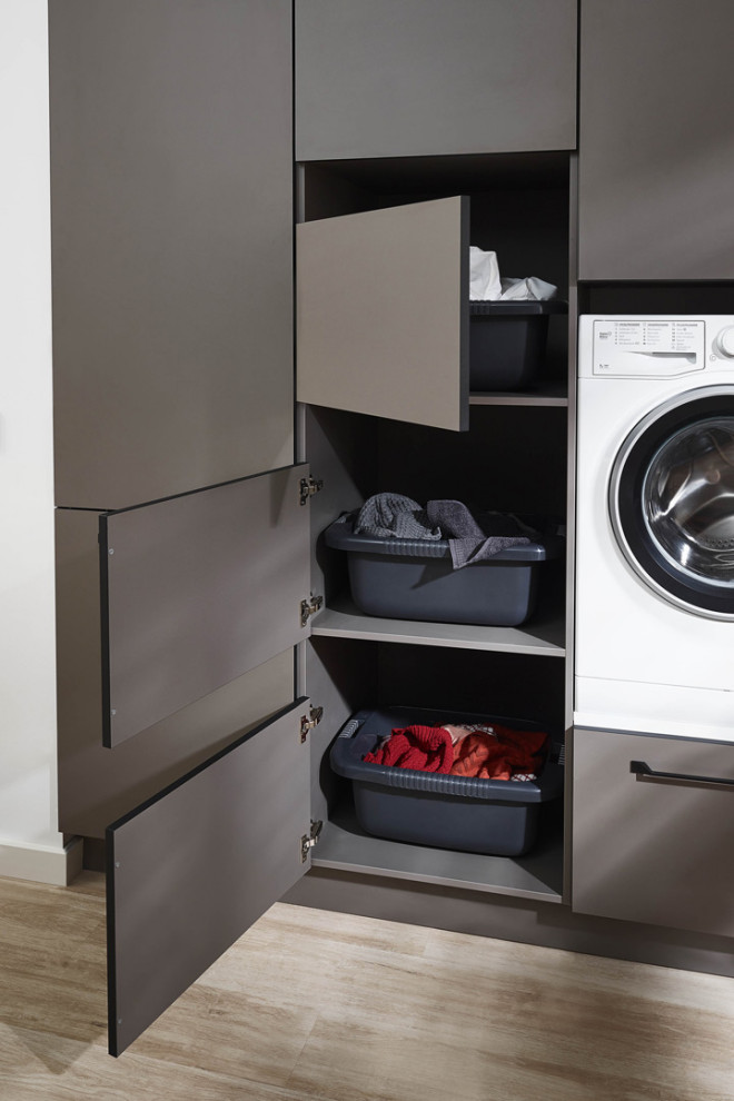 Photo of a mid-sized scandinavian l-shaped laundry cupboard in Miami with flat-panel cabinets, grey cabinets, laminate benchtops, white walls, laminate floors, an integrated washer and dryer, beige floor and grey benchtop.
