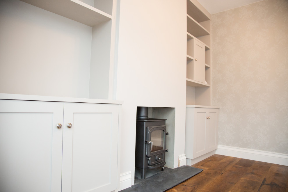 Inspiration for a mid-sized traditional formal enclosed living room in London with beige walls, dark hardwood floors, a wood stove, a plaster fireplace surround and brown floor.