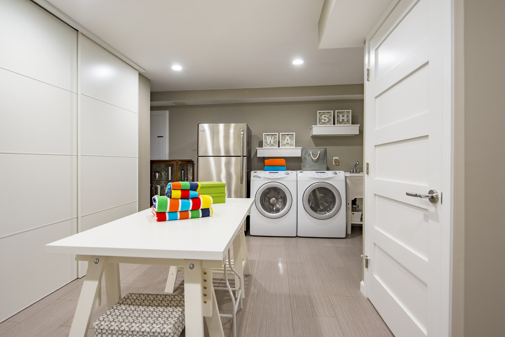 Large contemporary utility room in DC Metro with grey walls, a side-by-side washer and dryer, grey floor and laminate floors.