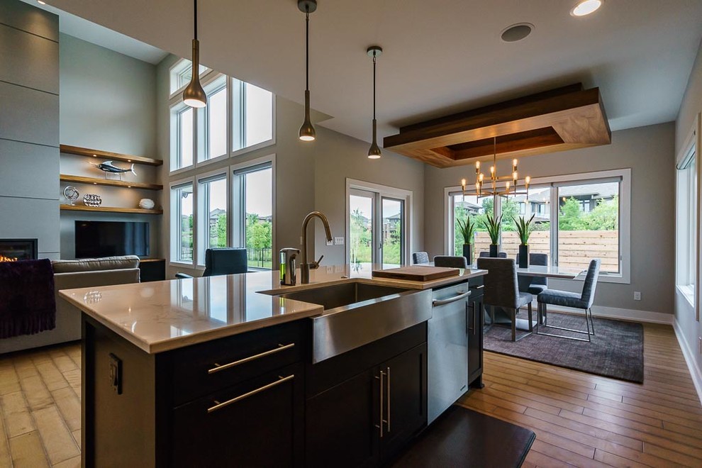 Photo of a mid-sized contemporary open plan kitchen in Omaha with a farmhouse sink, shaker cabinets, black cabinets, granite benchtops, bamboo floors, with island, beige floor and beige benchtop.