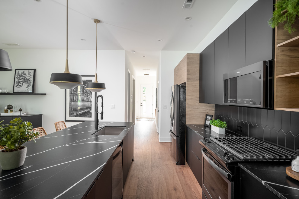 Inspiration for a contemporary galley kitchen in Charlotte with an undermount sink, flat-panel cabinets, quartz benchtops, ceramic splashback, stainless steel appliances, laminate floors, with island, black cabinets, black splashback and black benchtop.